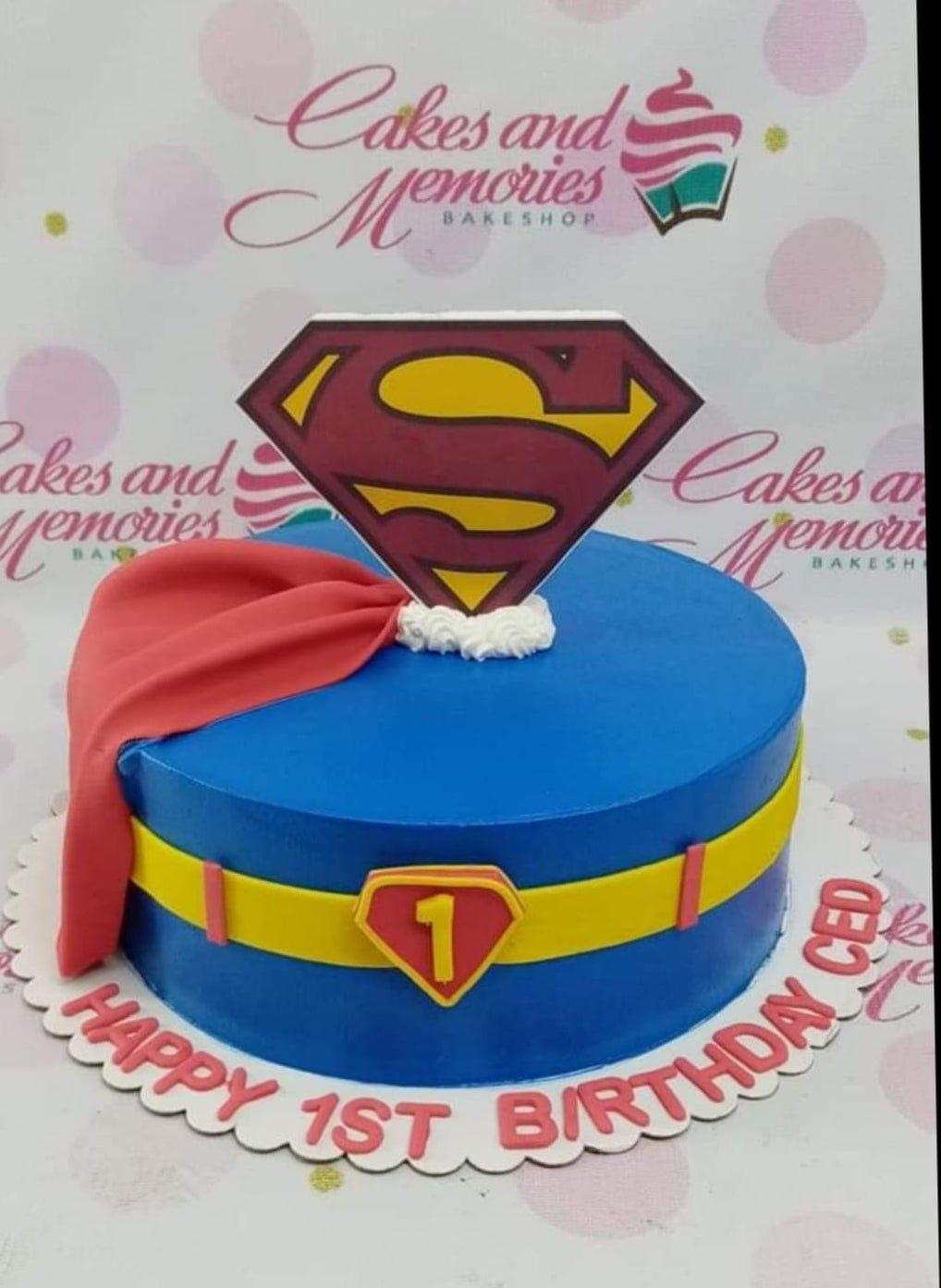 Superman themed blue birthday cake with a red fondant cape, yellow belt, and a large Superman logo topper.
