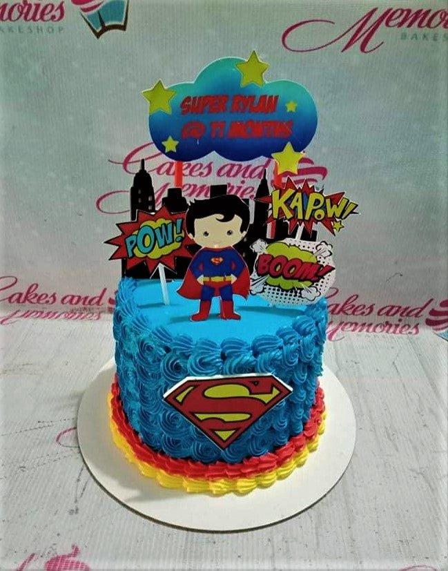 Blue Superman themed birthday cake with blue icing rosettes, red and yellow borders, and superhero printout toppers.