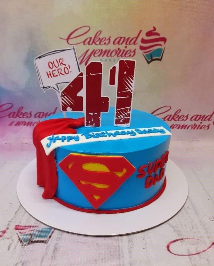 Blue Superman themed birthday cake for Dad with a red fondant cape and Superman logo on the side.