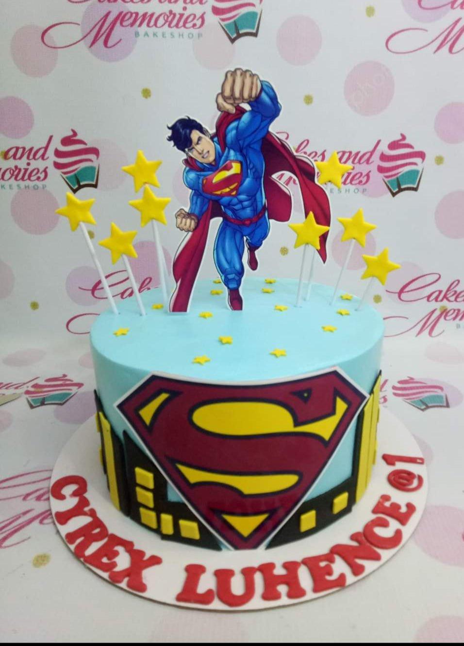 Light blue Superman themed birthday cake with a flying Superman cutout, yellow stars, and a city skyline silhouette.