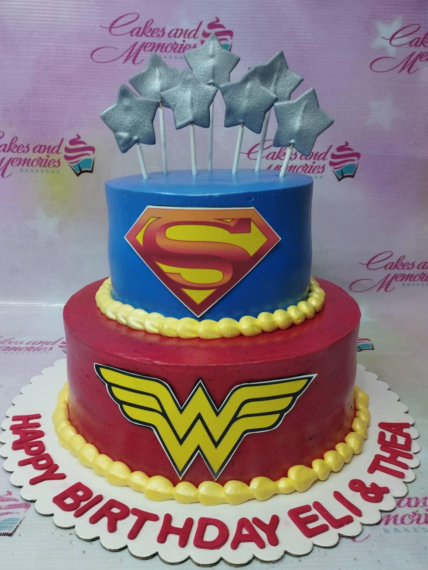 Two-tier Superman and Wonder Woman themed birthday cake in blue and red with silver stars and yellow icing borders.