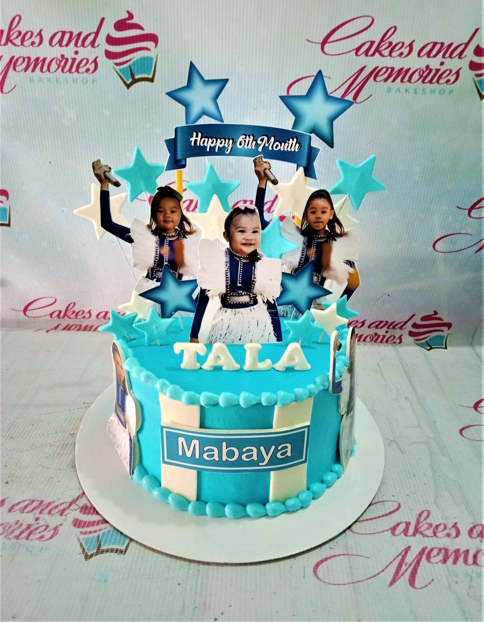 Light blue 6th month birthday cake for Tala Mabaya featuring photo printouts of a baby girl and blue and white stars.