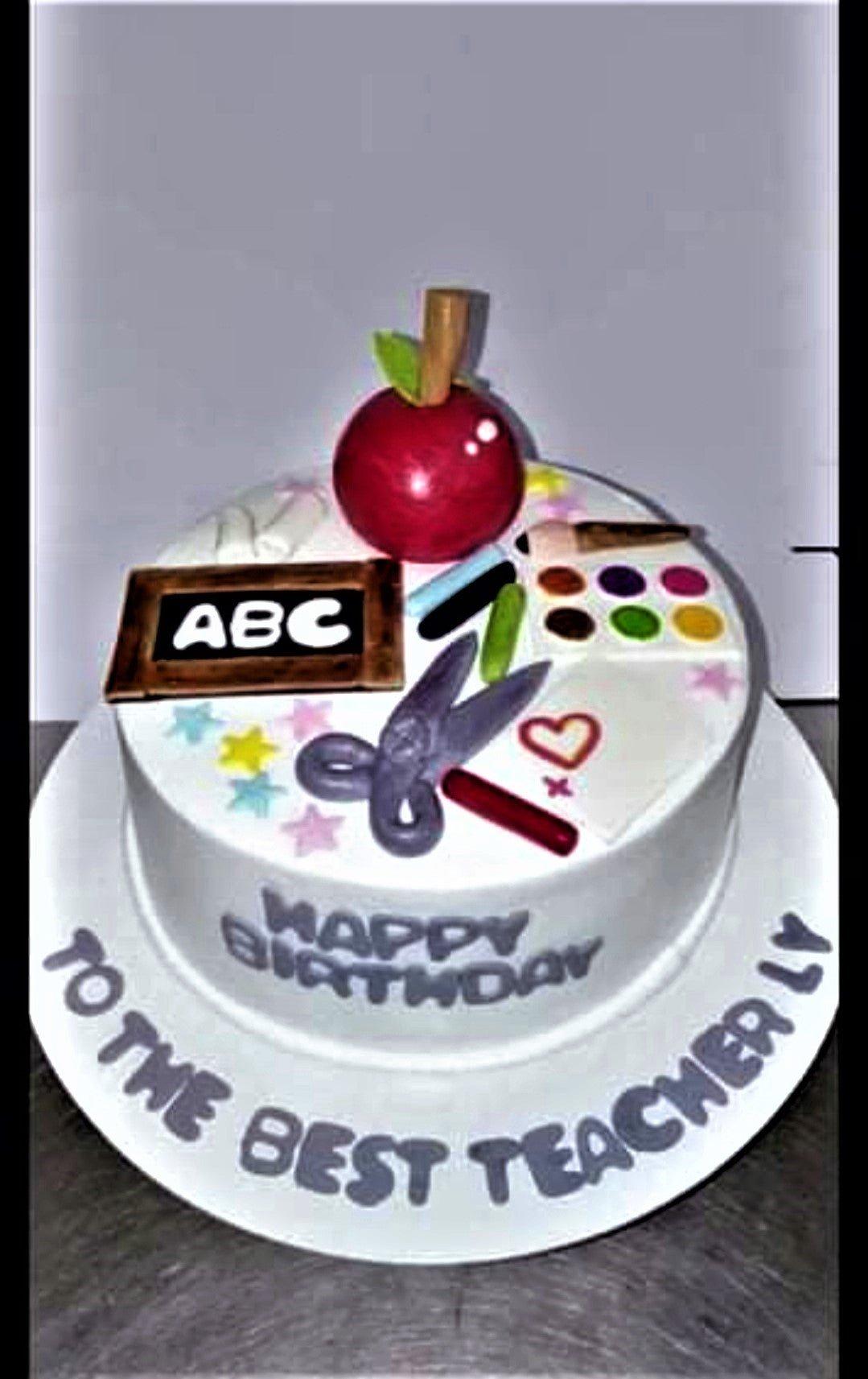 White round teacher-themed birthday cake with a large red fondant apple, school supplies, and a chalkboard topper.