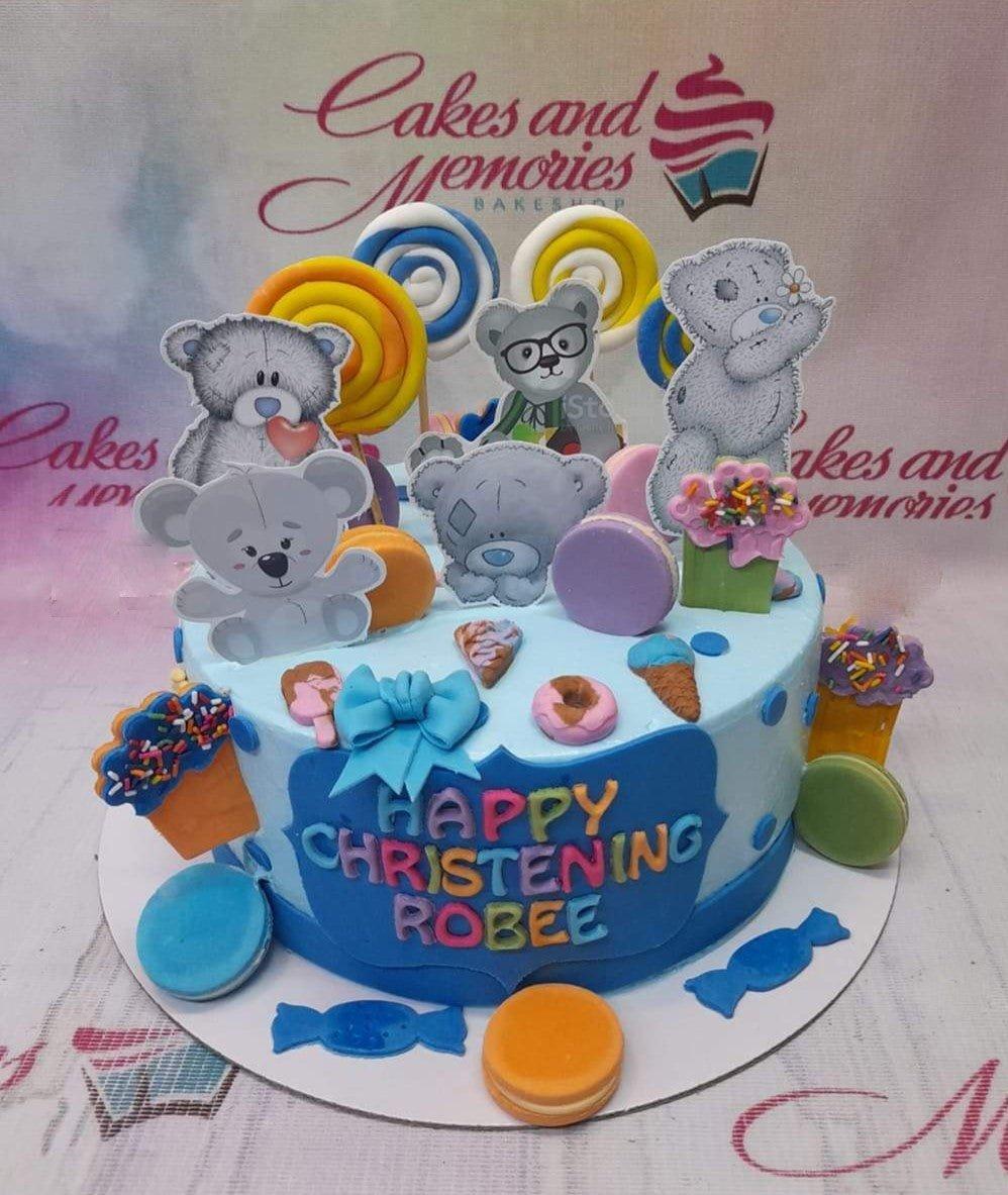 Light blue christening cake for Robee featuring grey teddy bear printouts, colorful fondant lollipops, and sweet treats like donuts and ice cream.