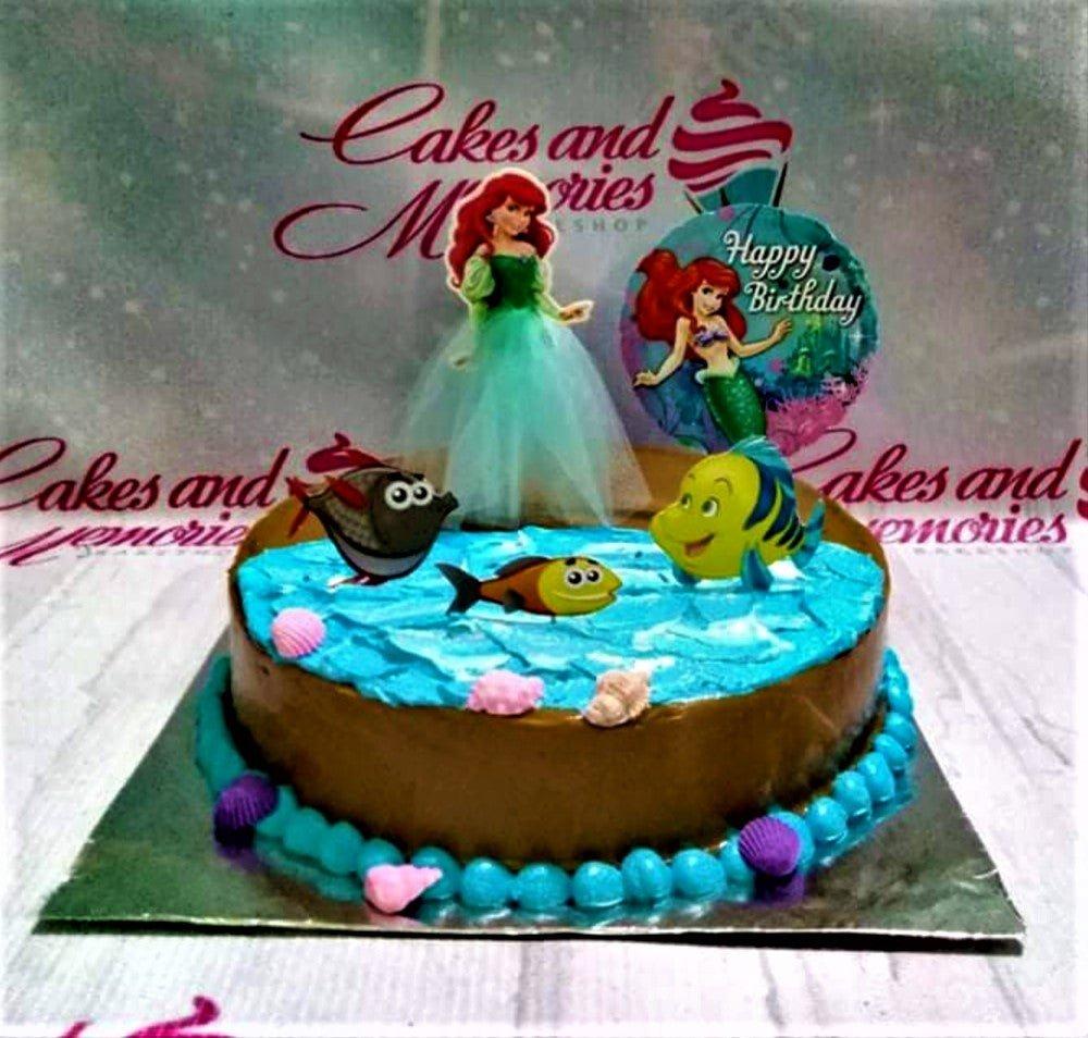 The Little Mermaid themed chocolate cake with Ariel and Flounder printout toppers and blue icing waves.