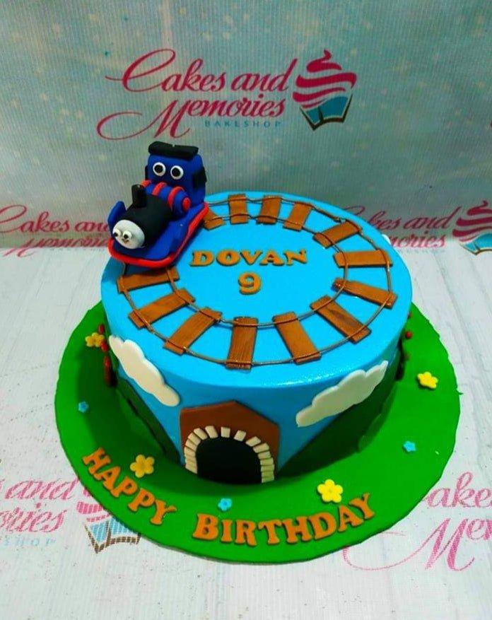 Blue Thomas the Train themed birthday cake with a fondant train on a track and a green base board.