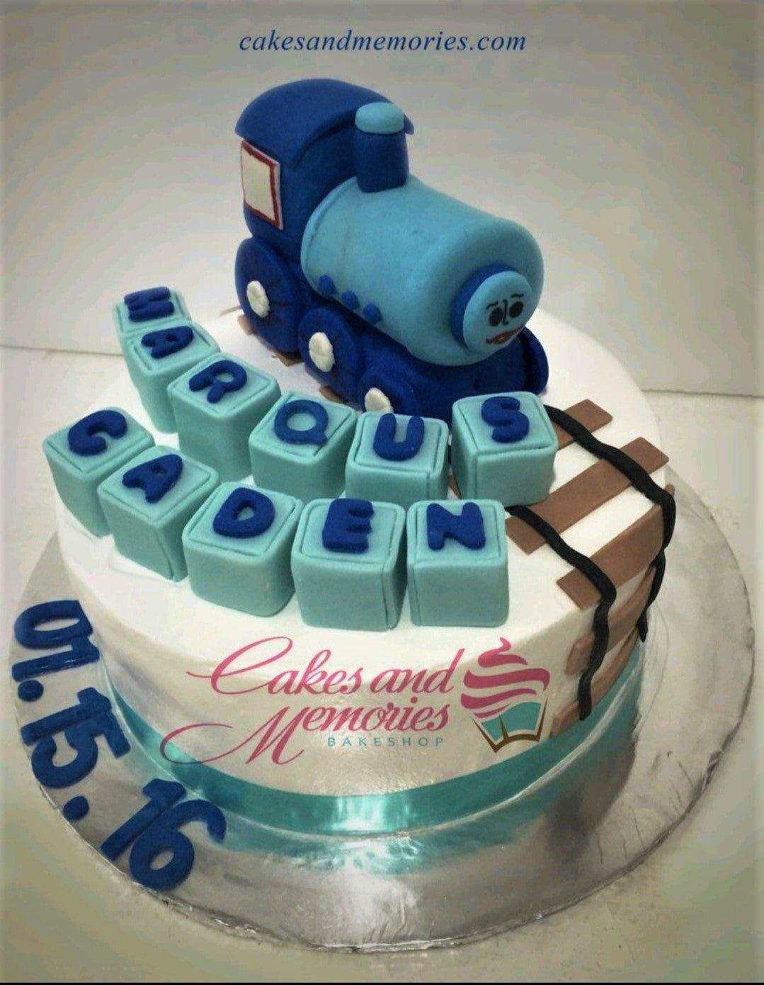 Blue and white Thomas the Train themed fondant cake with a 3D train topper, name blocks, and train tracks.