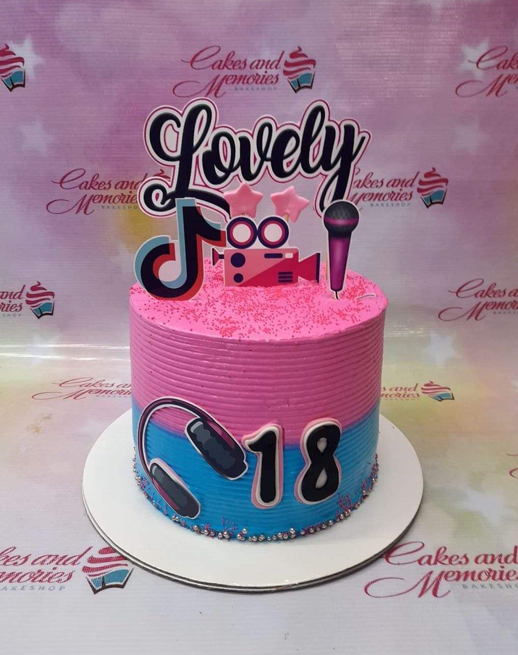 Pink and blue 18th birthday cake with TikTok, camera, microphone, and headphone printout toppers and silver dragees.