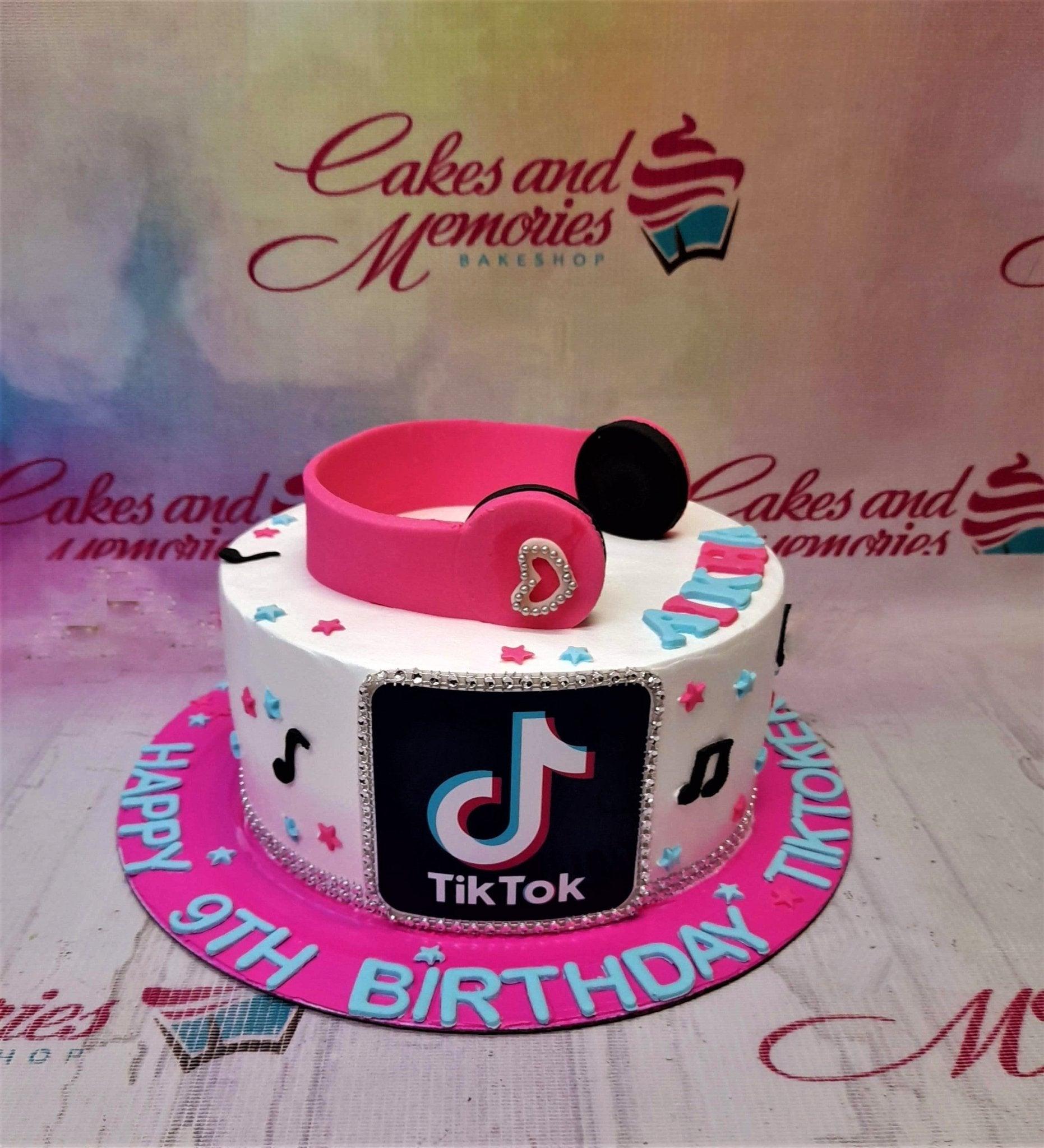 White TikTok themed birthday cake with pink headphones topper, music notes, and stars on a hot pink base board.