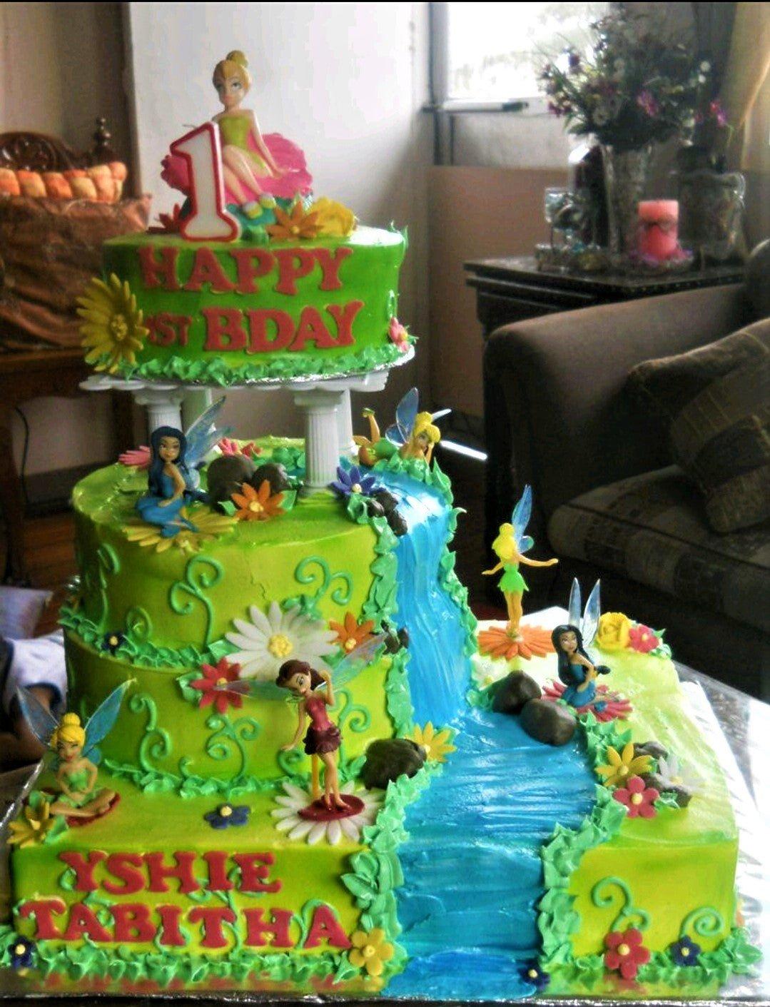 Three-tier Tinkerbell and fairies themed birthday cake with a blue icing waterfall, green grass textures, and colorful fondant flowers.