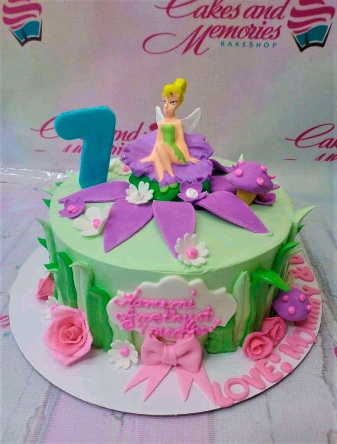 Light green Tinkerbell themed cake with a 3D fairy figure, purple fondant petals, pink roses, and a blue number 7 topper.