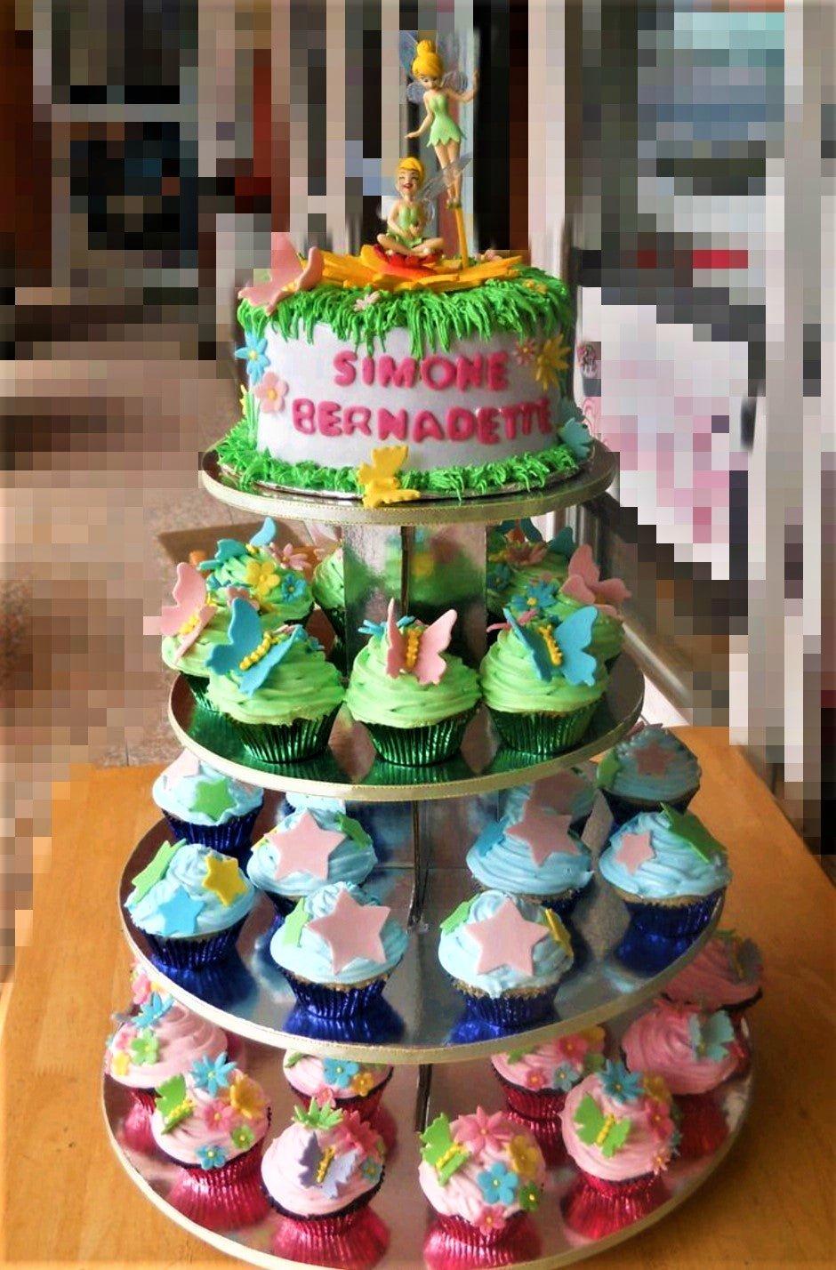 Tinkerbell themed birthday cake with green grass icing, pink and blue flowers, and Tinkerbell figurines on a multi-tier cupcake stand.