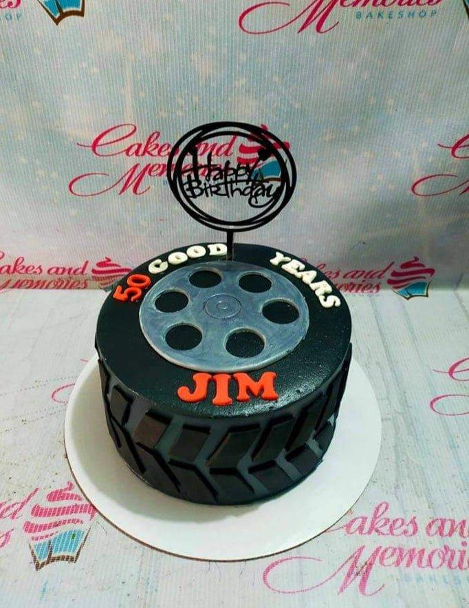 Black tire-shaped birthday cake for Jim's 50th birthday with a film reel design and a Happy Birthday topper.