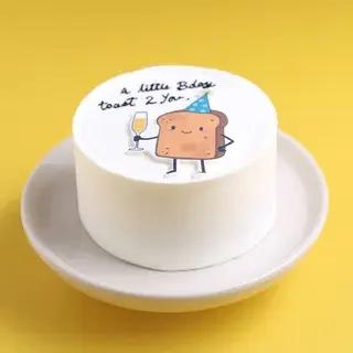 White bento cake with a cute toast character printout wearing a party hat and holding a glass of champagne.