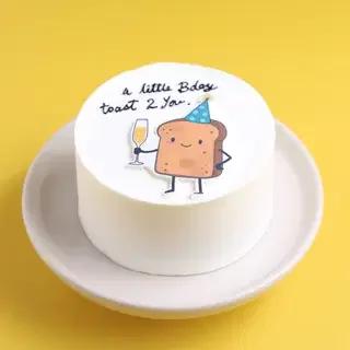 White bento cake with a cute toast character printout wearing a party hat and holding a glass of champagne.