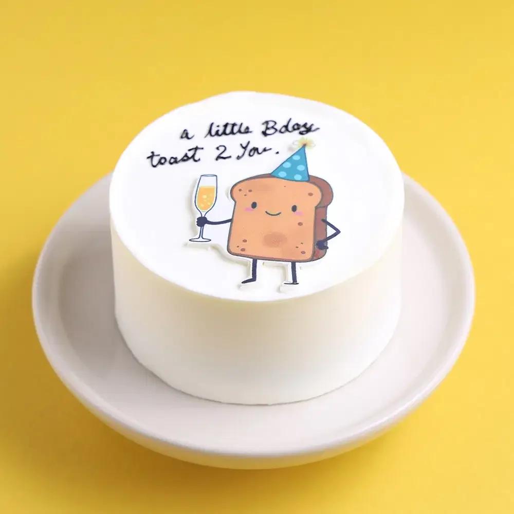 White bento cake with a cute toast character wearing a party hat and holding a champagne glass with a birthday message.