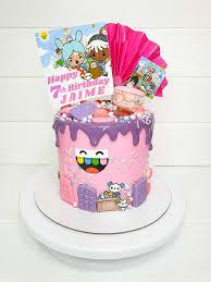 Pink Toca Boca themed birthday cake with purple drip, character printouts, and colorful chocolate bar decorations.