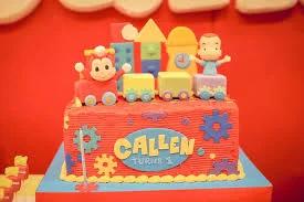 Red rectangle birthday cake with a colorful toy train topper and fondant gear decorations for Callen's 1st birthday.