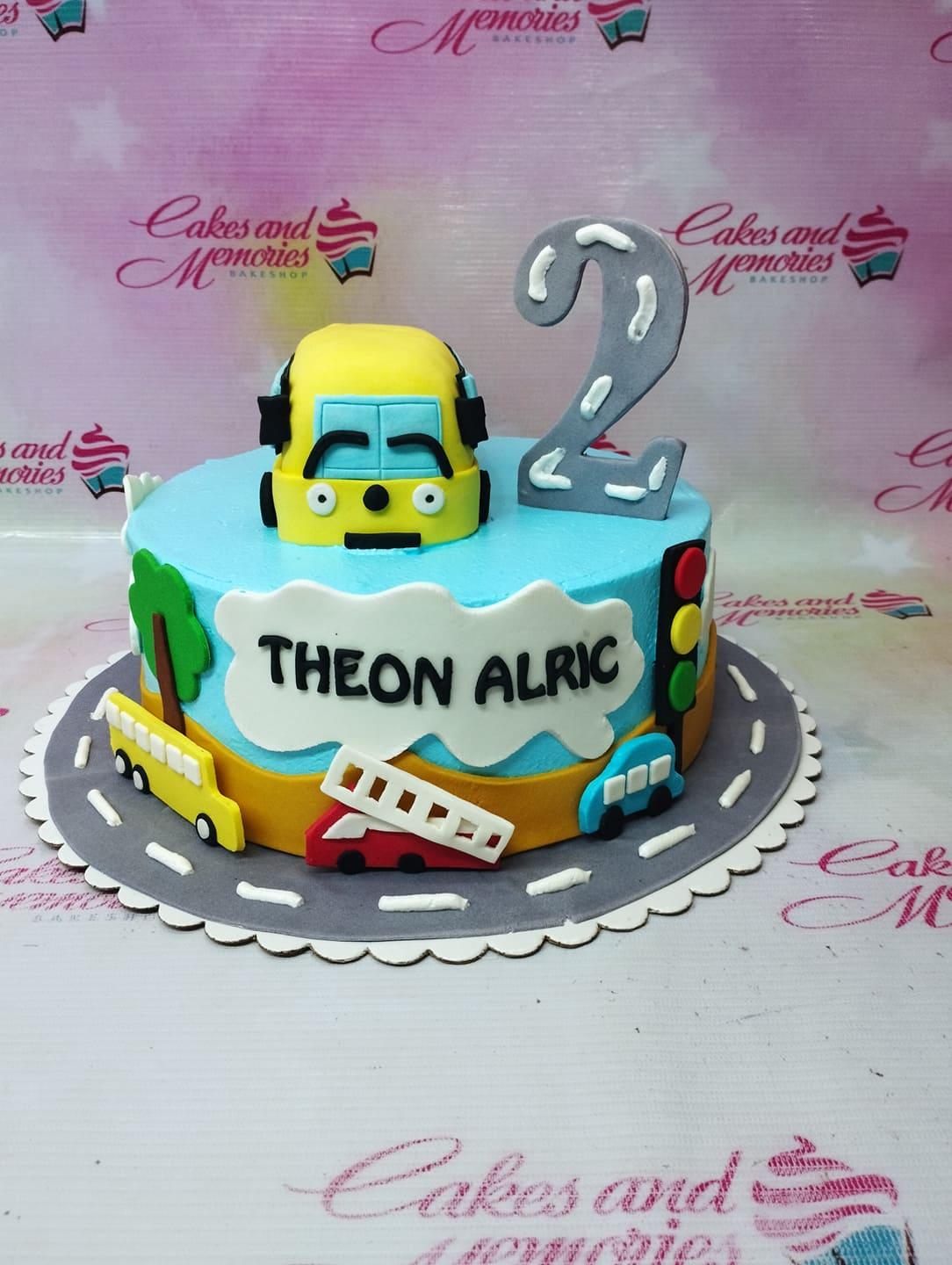 Blue and yellow transportation themed birthday cake with a bus topper, traffic light, and road design for a 2nd birthday.