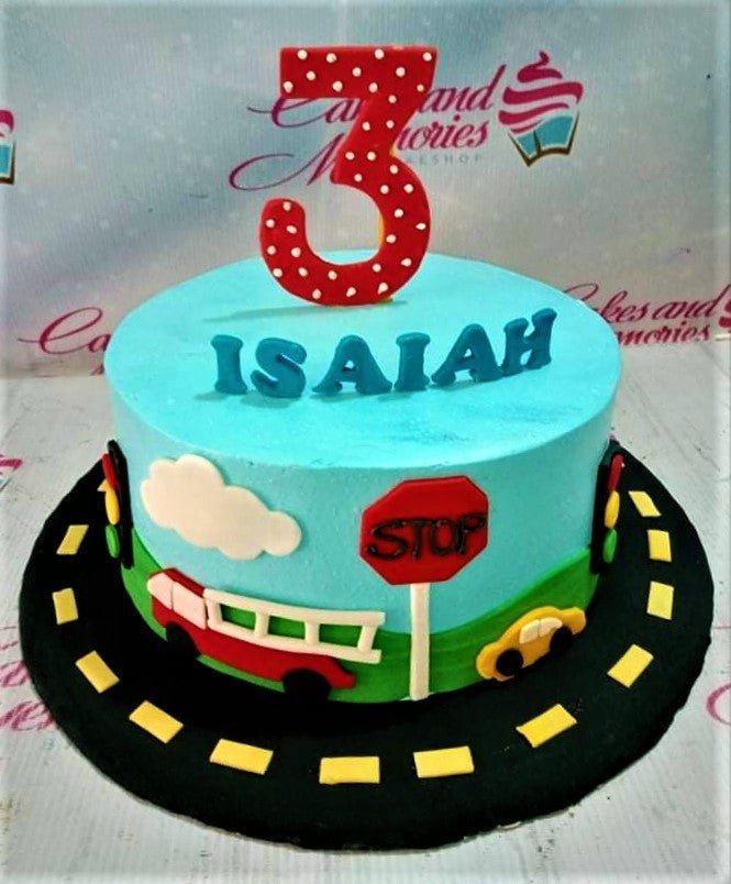 Light blue transportation themed birthday cake with a red fire truck, yellow car, stop sign, and a large red number three topper.
