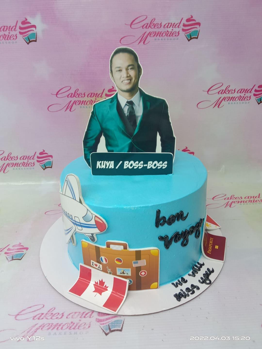 Light blue travel themed cake with a photo printout of a man in a suit, an airplane, a suitcase, and various flags.