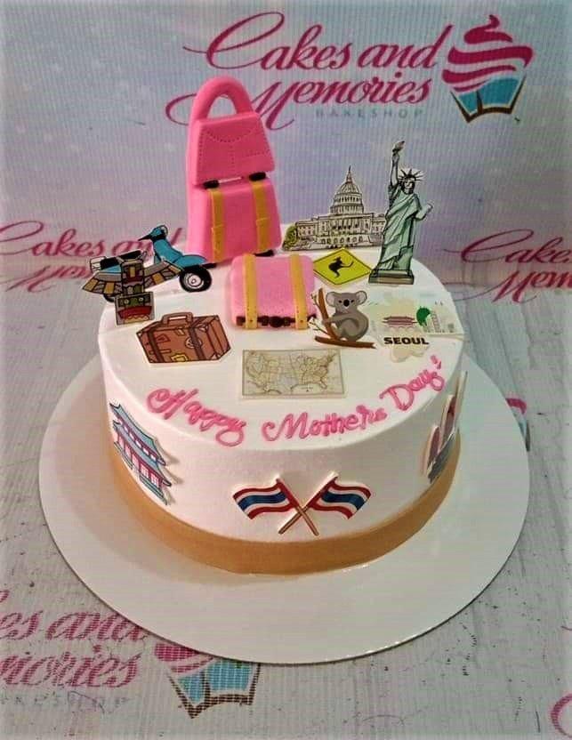 White travel-themed Mother's Day cake with pink luggage toppers, world landmarks, and a Happy Mother's Day message.