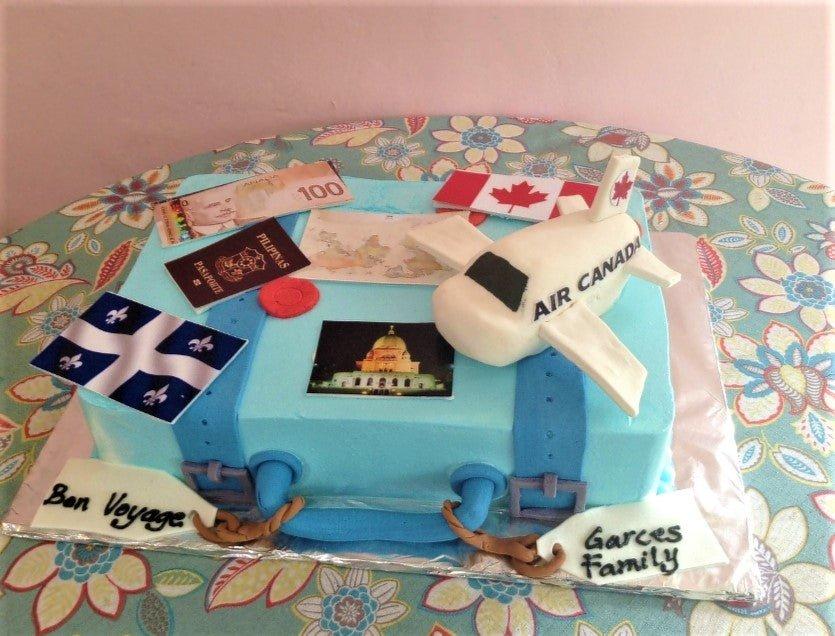 Light blue square suitcase cake with a 3D fondant airplane, Canadian flag, passport, and travel-themed printouts.