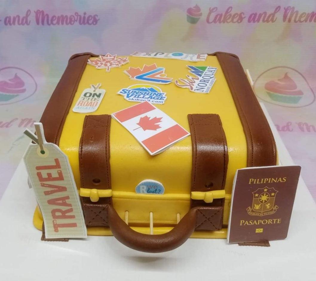Yellow suitcase-shaped fondant cake with travel stickers, a Philippine passport, and a Canadian flag topper.