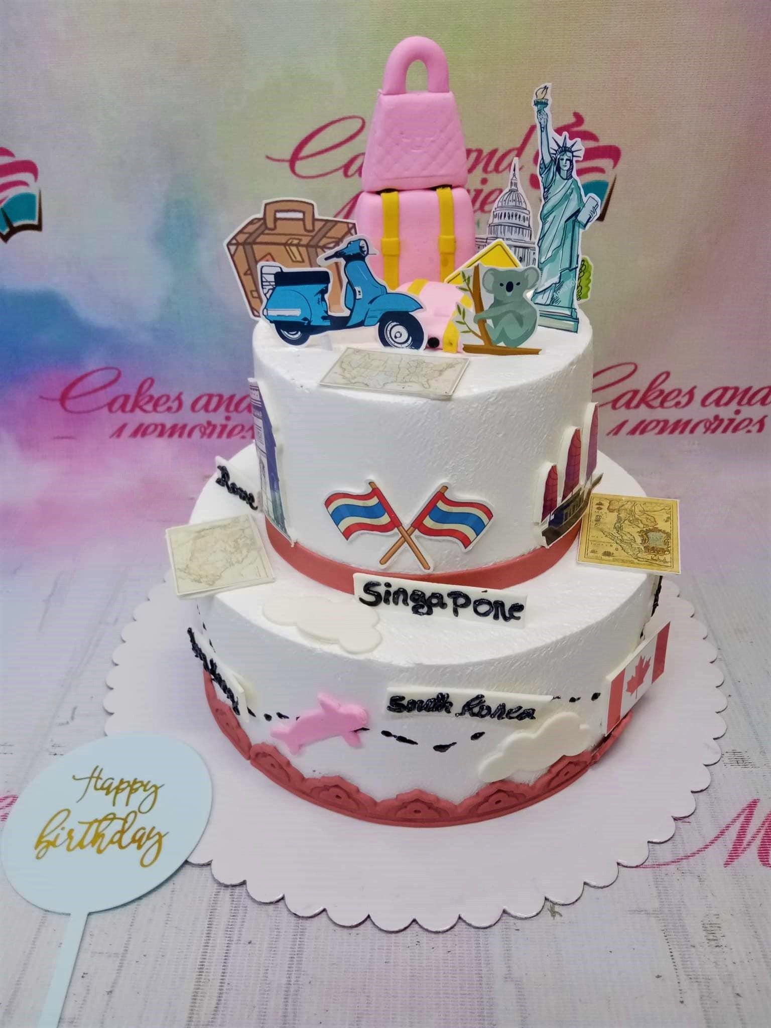White 2-tier travel themed cake with pink luggage, blue scooter, and world landmark printouts including Statue of Liberty and flags.