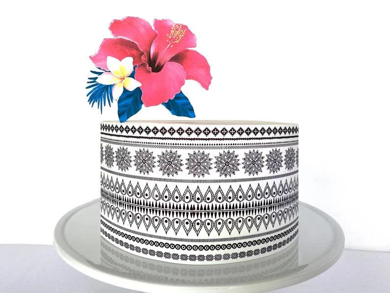 White single tier cake with black tribal mandala patterns and a large pink hibiscus flower topper with blue tropical leaves.