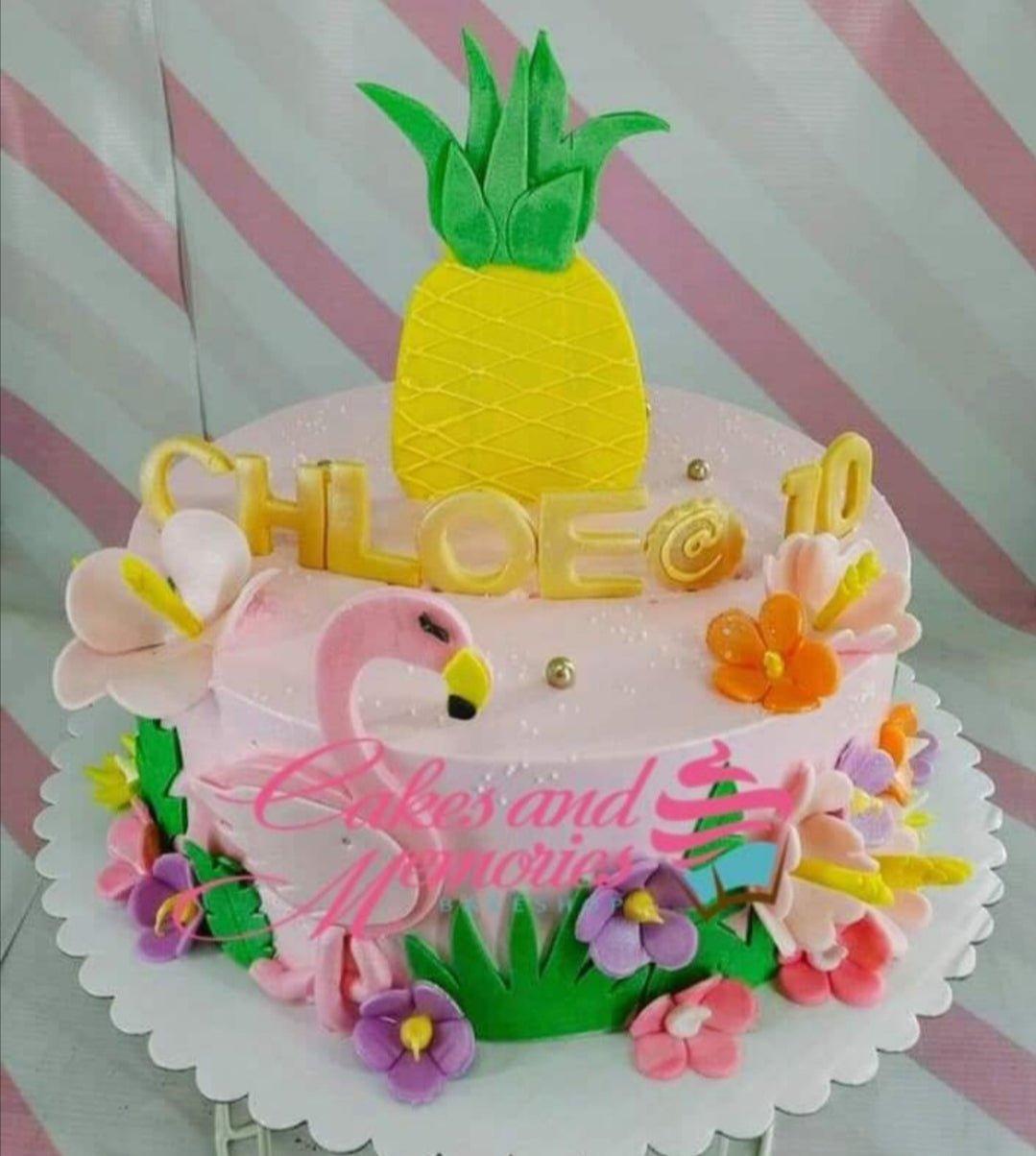Pink tropical flamingo and pineapple birthday cake with edible flowers and gold name topper