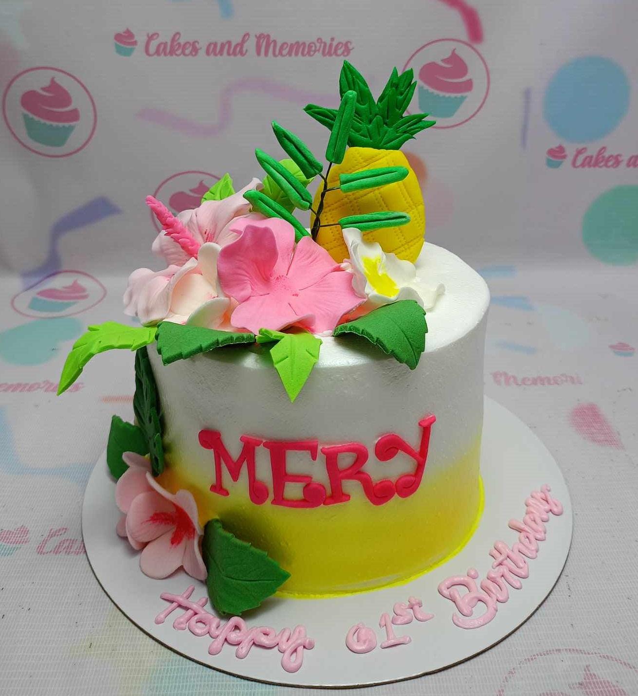 Tropical themed white and yellow gradient cake with pink hibiscus flowers, green leaves, and a 3D fondant pineapple topper.