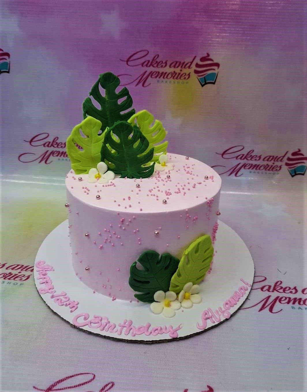 Pink tropical birthday cake with green monstera leaves, white flowers, and pink sprinkles.