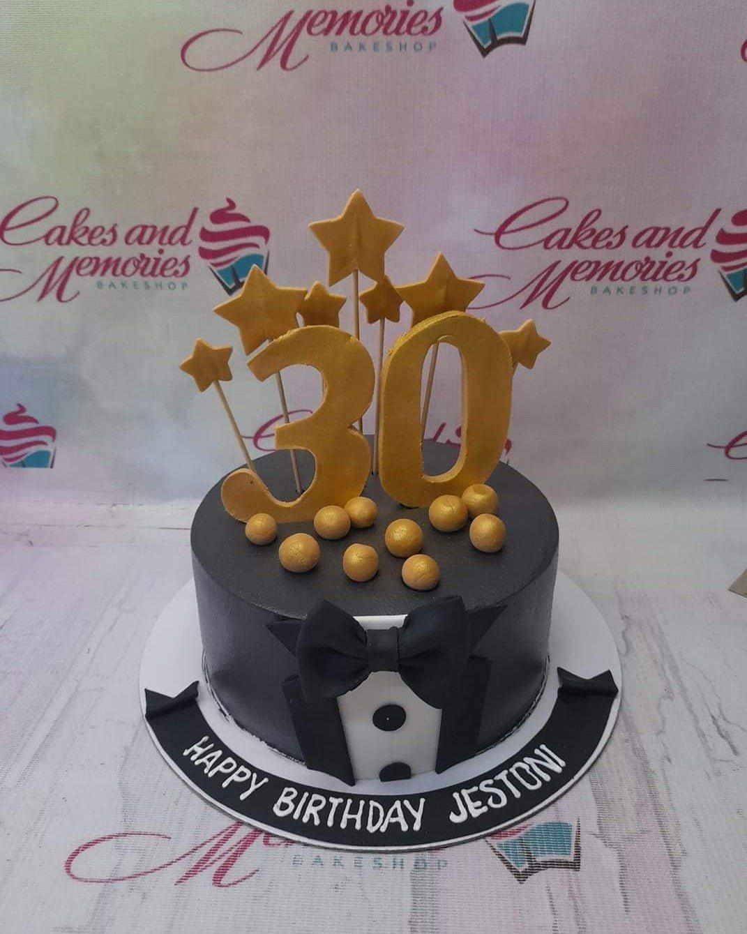 Black tuxedo themed 30th birthday cake with gold number 30 and star toppers on a black fondant base.