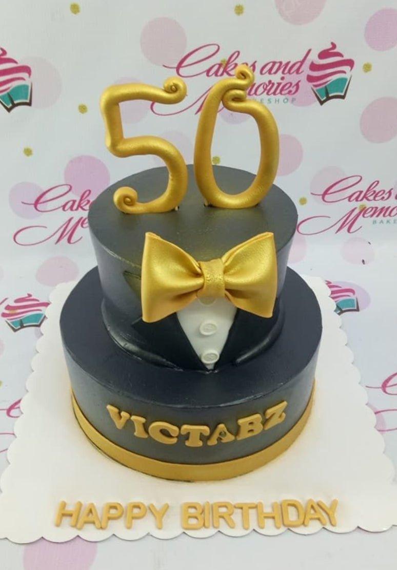 Two-tier black tuxedo birthday cake with a gold bow tie and gold number 50 topper.