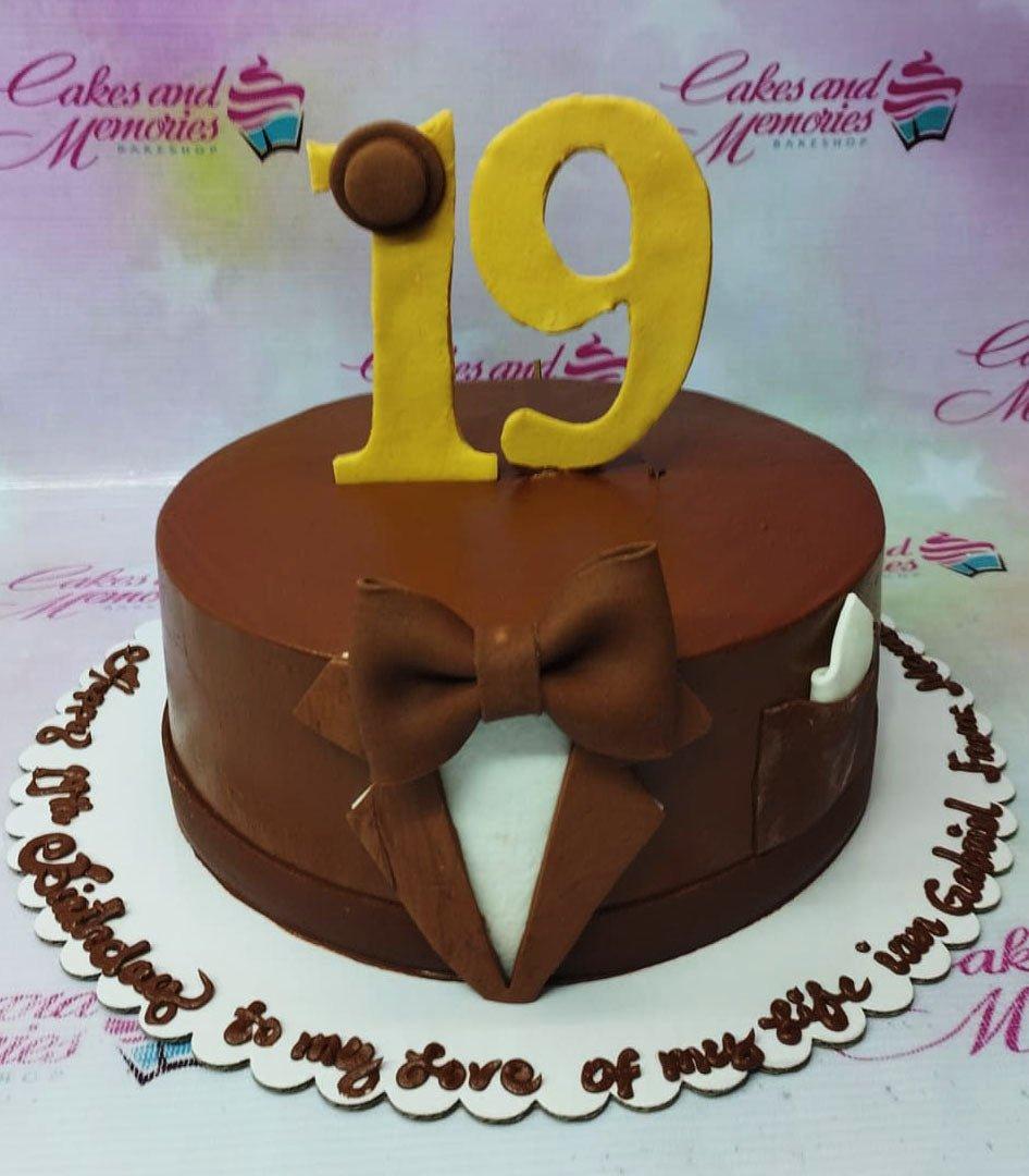 Brown tuxedo-themed birthday cake with a large yellow number 19 topper and a fondant bow tie.