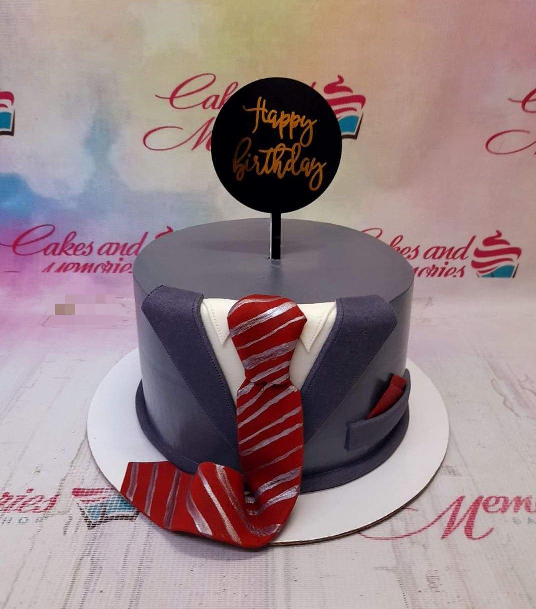 Gray tuxedo fondant cake with a red and silver striped tie and a black Happy Birthday topper.