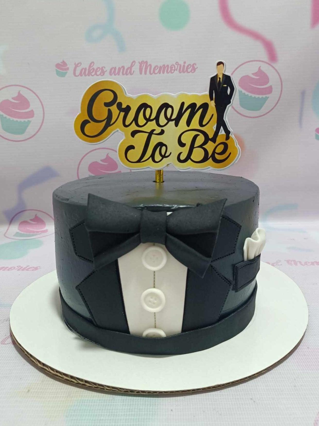 Black tuxedo themed groom-to-be cake with a black bow tie, white shirt panel, and a Groom To Be printout topper.