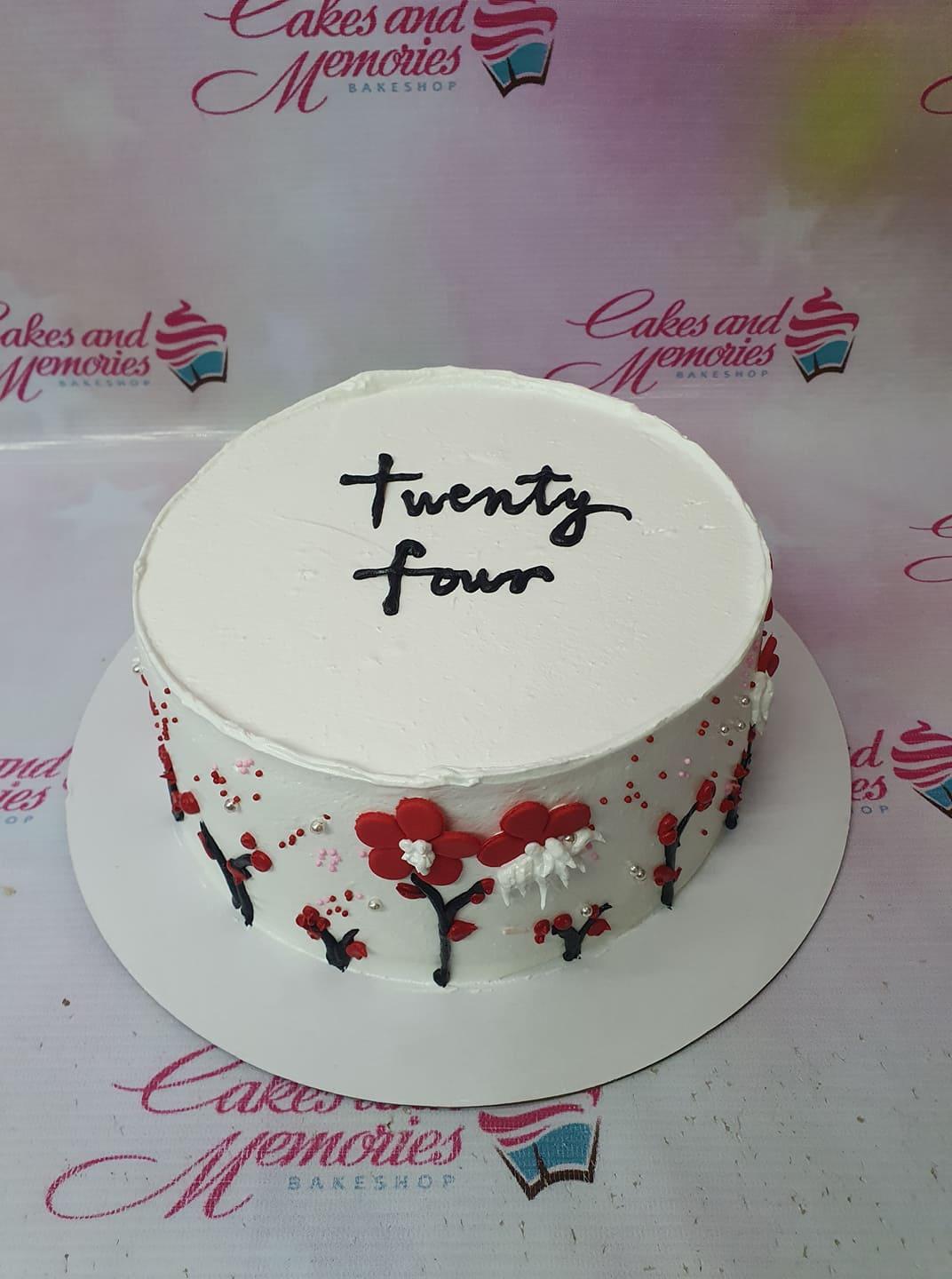 White minimalist cake with black cursive 'twenty four' message and red floral icing decorations on the sides.