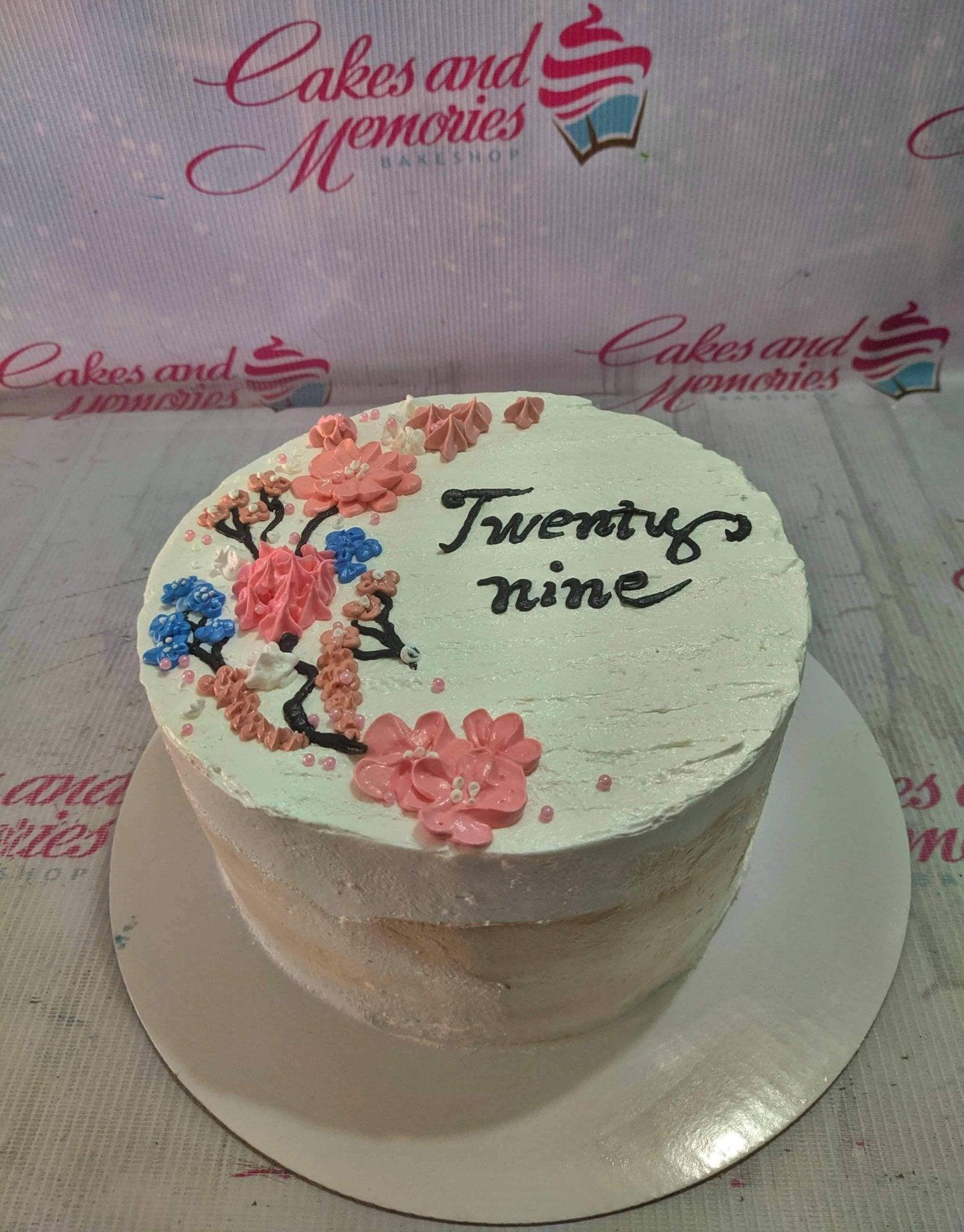 White minimalist cake with pink and blue palette knife icing flowers and black piped text reading Twenty nine.