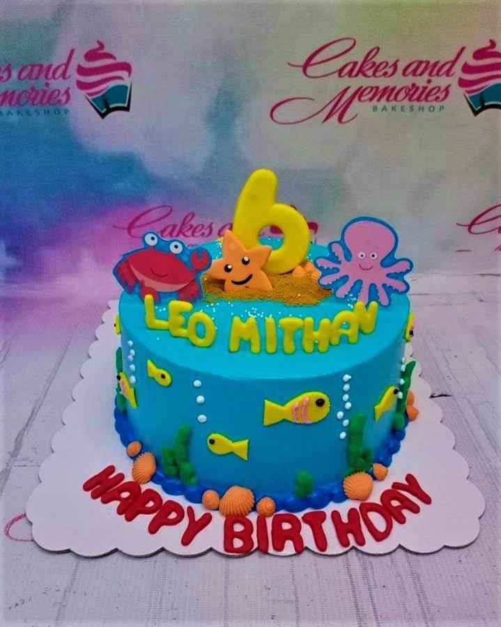 Under the sea themed birthday cake in blue icing with fondant crab, octopus, starfish, and yellow fish decorations.