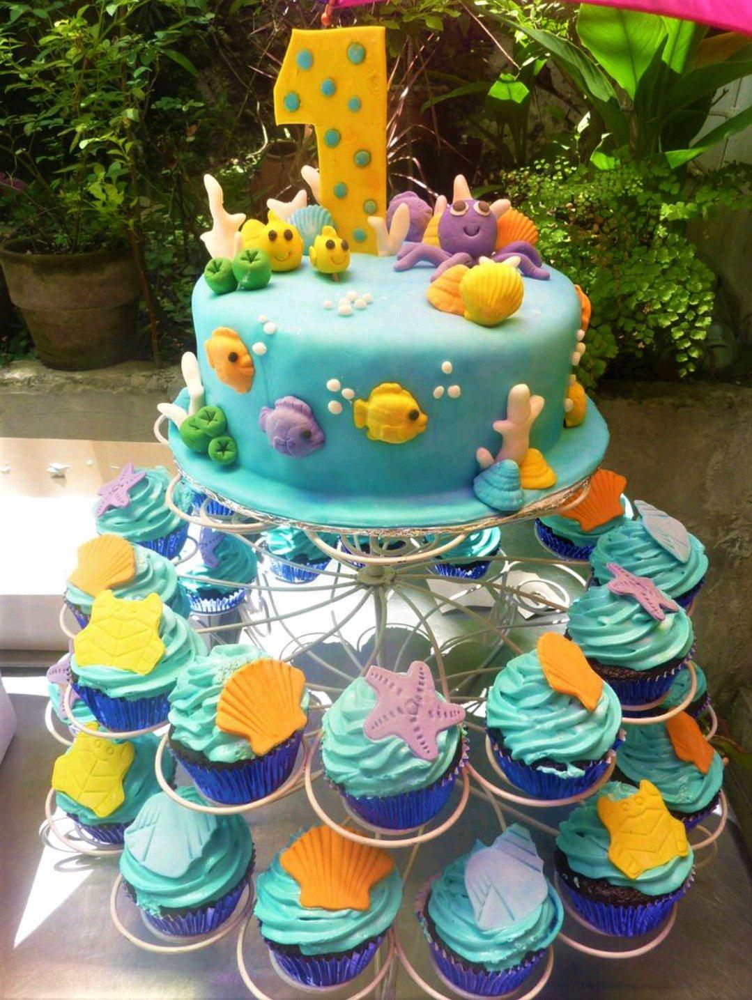 Under the sea themed blue fondant cake with edible 3D sea creatures like an octopus, fish, and shells, displayed on a cupcake stand.