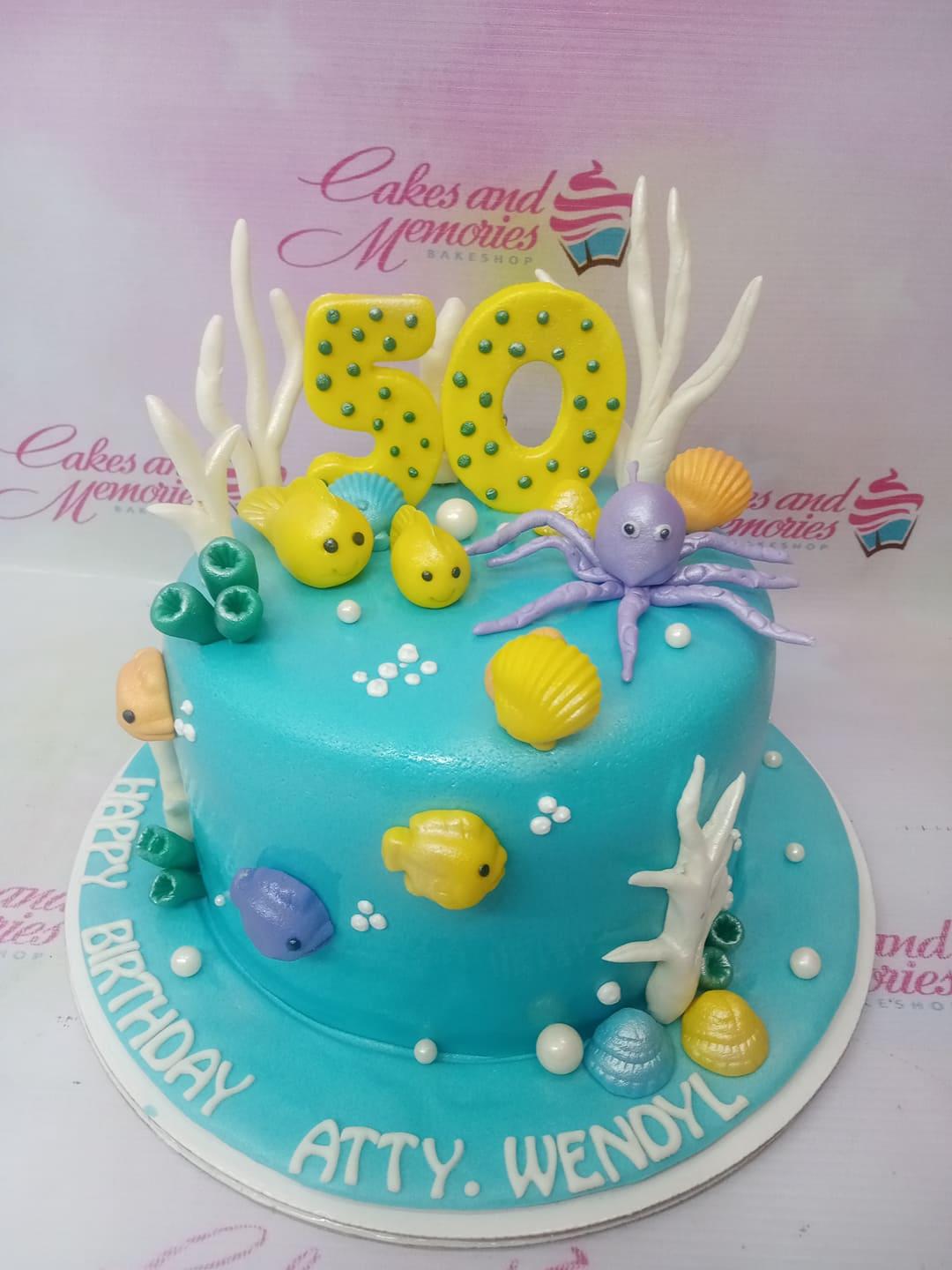 Under the sea themed blue fondant cake with 3D edible sea creatures, coral, and a yellow number 50 topper.