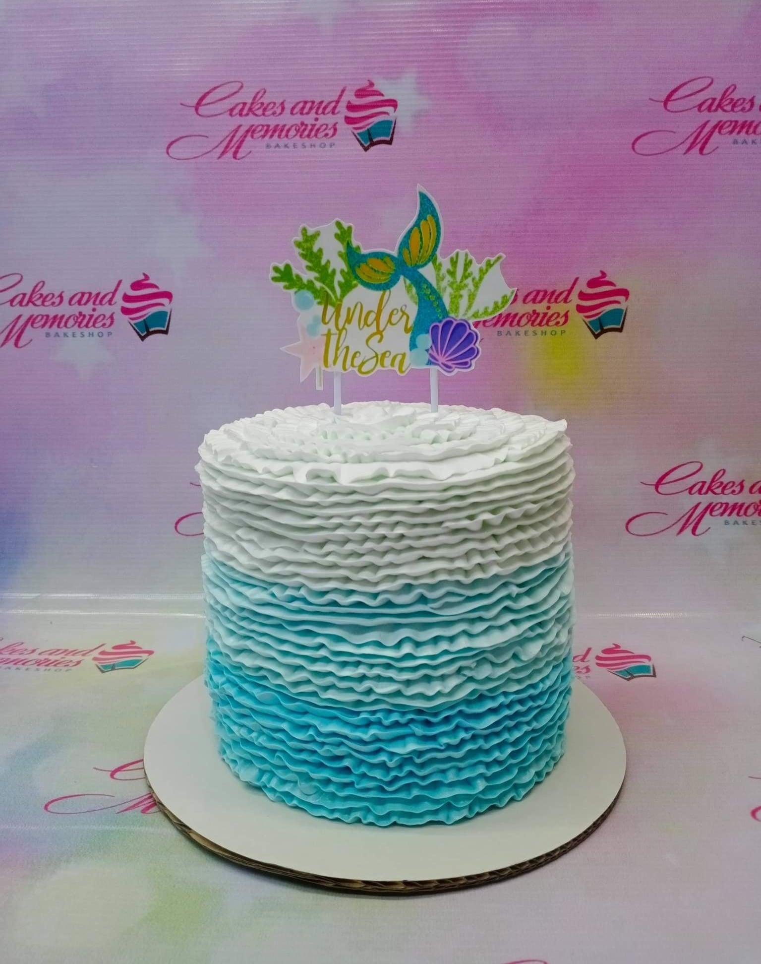 Under the Sea themed cake with blue and white ombre ruffles and a mermaid tail topper.