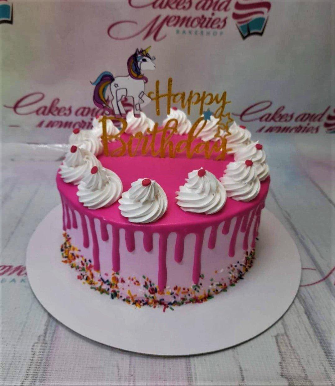 Pink unicorn birthday cake with hot pink drip, white icing rosettes, and a gold glitter Happy Birthday topper.
