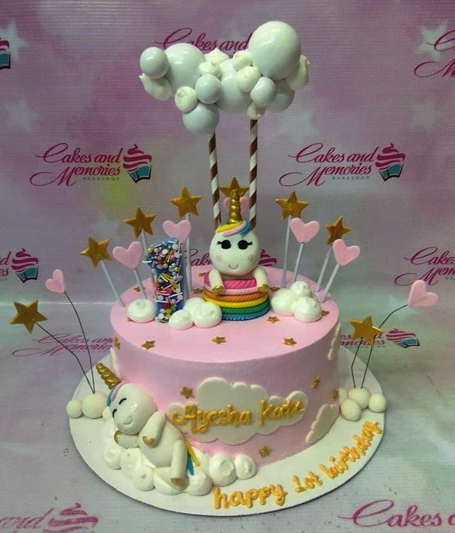 Pink unicorn birthday cake with rainbow accents, fondant clouds, and gold stars for a first birthday celebration.
