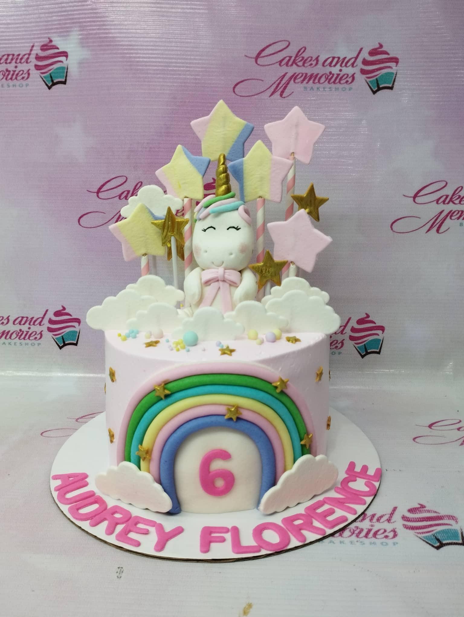 Pink unicorn birthday cake with a fondant unicorn topper, rainbow arch, and pastel stars on a white base board.