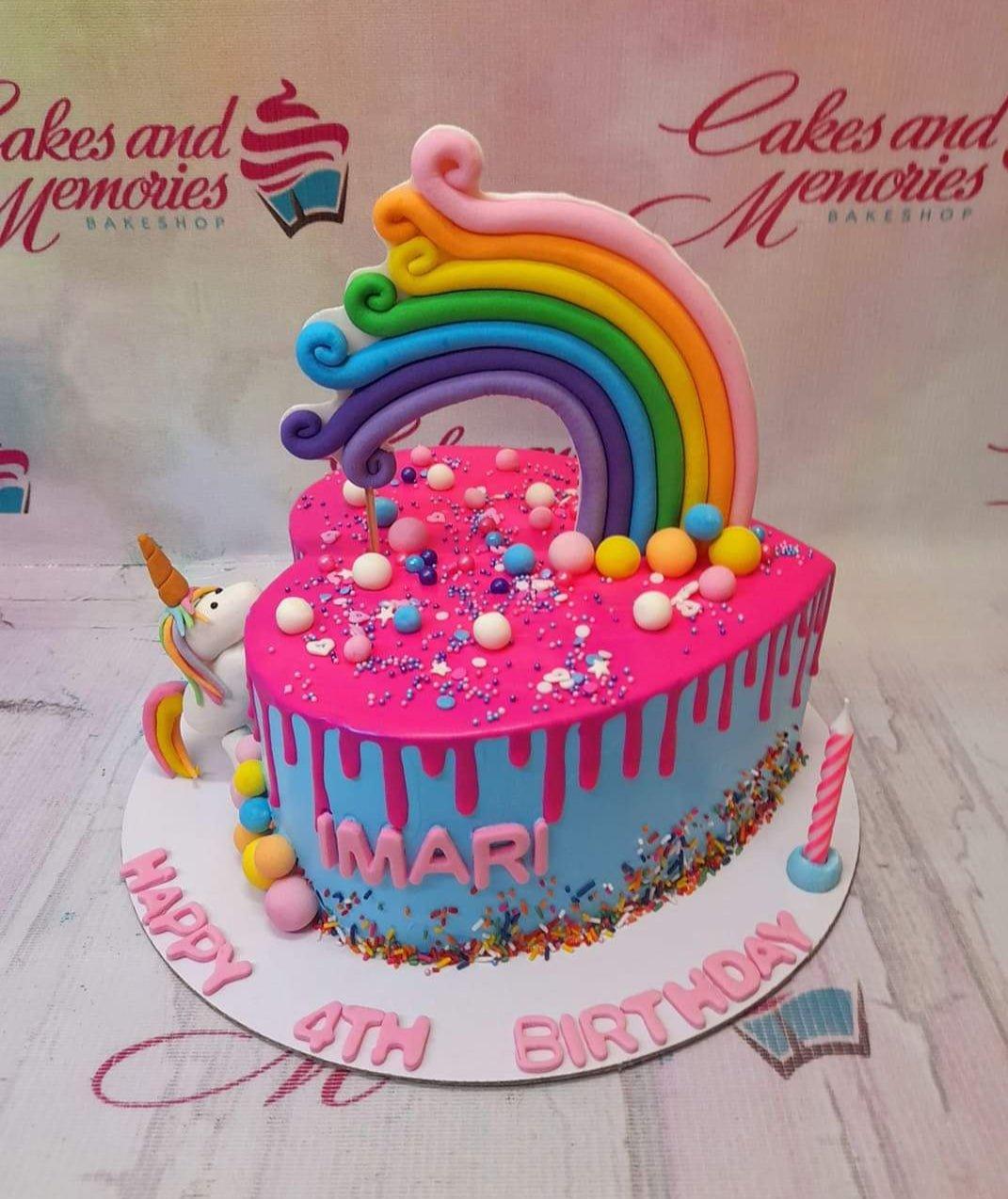 Heart-shaped blue cake with pink drip, rainbow topper, and a fondant unicorn figure.