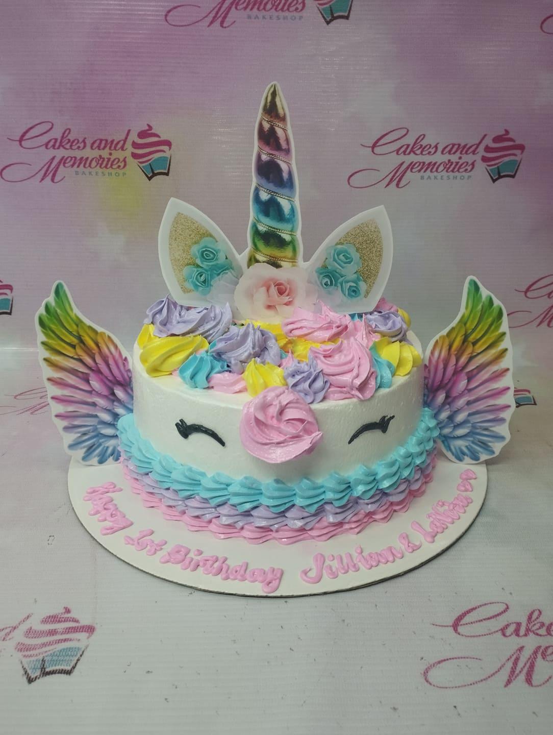 White unicorn cake with colorful icing mane in pink, purple, yellow, and blue with printed unicorn horn and wings.