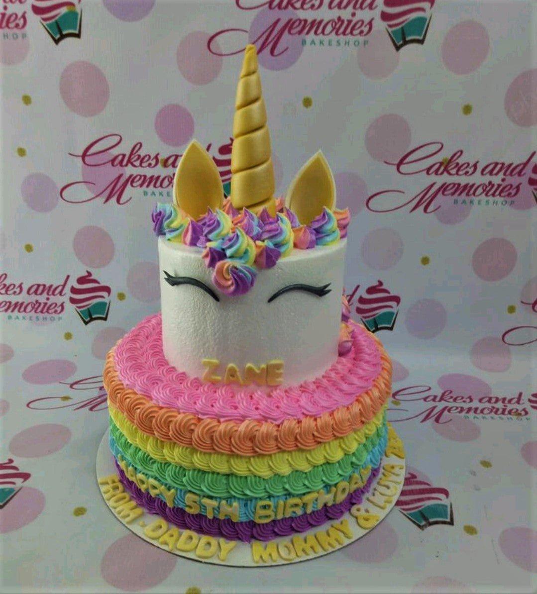 Two-tier rainbow unicorn cake with colorful icing ruffles, a gold horn, and personalized birthday messages.